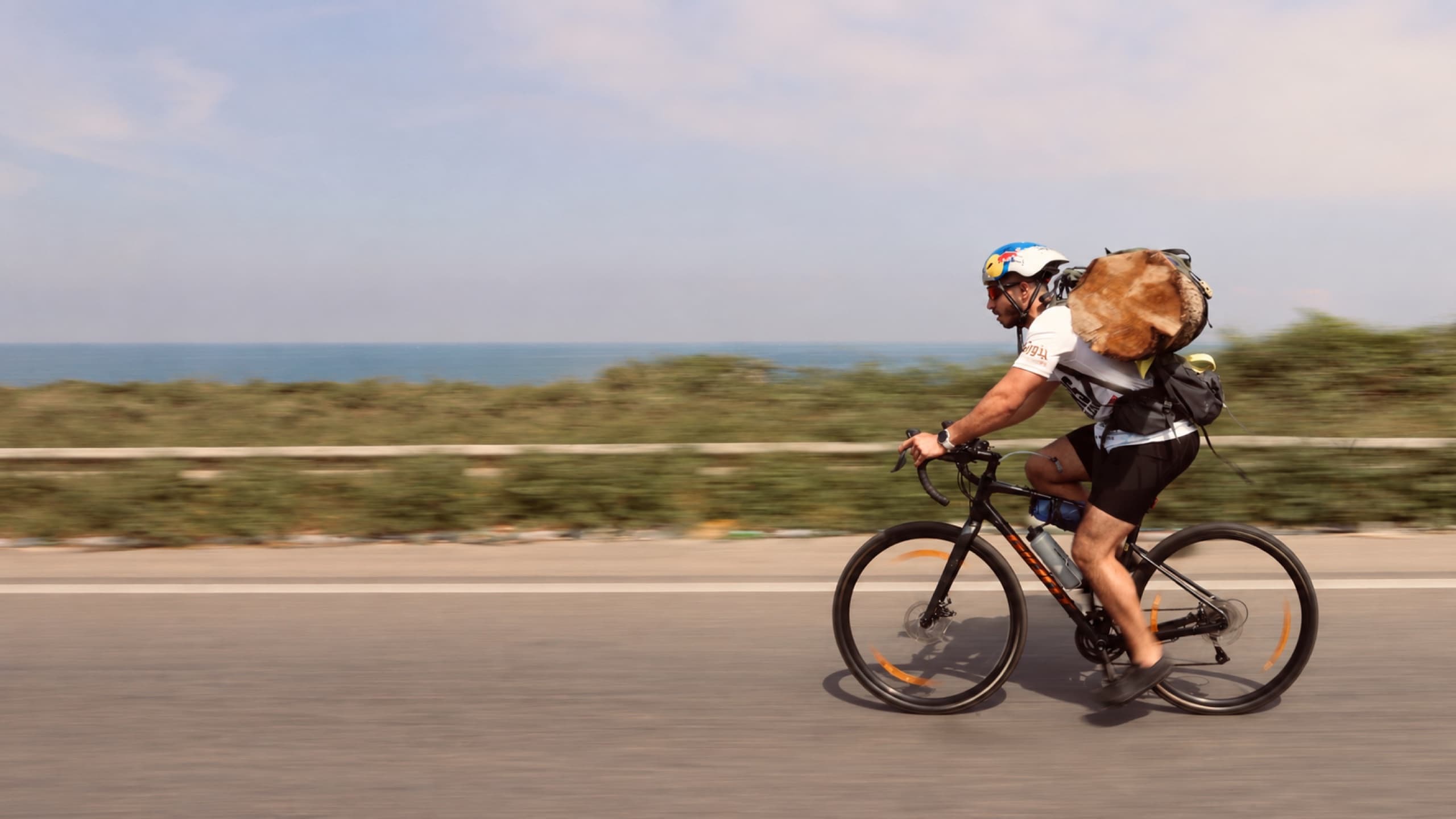 Joe Hachem cycling with a cedar log strapped to his back during the Cedars Treeathlon